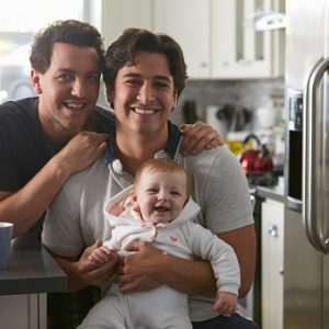 Male gay couple with baby girl in kitchen looking